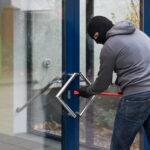 Hooded man using crowbar to open glass door